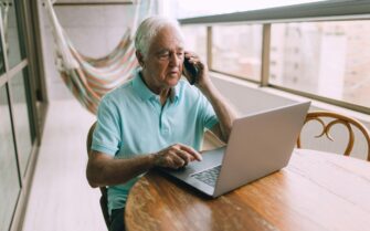 Un hombre mayor, hablando por teléfono y utilizando un ordenador.