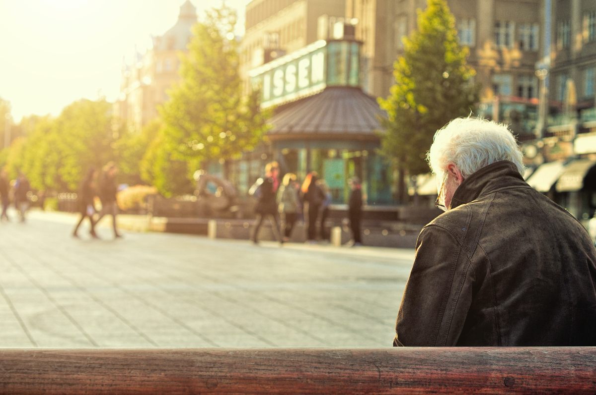 Un adulto mayor sentando en un banco.