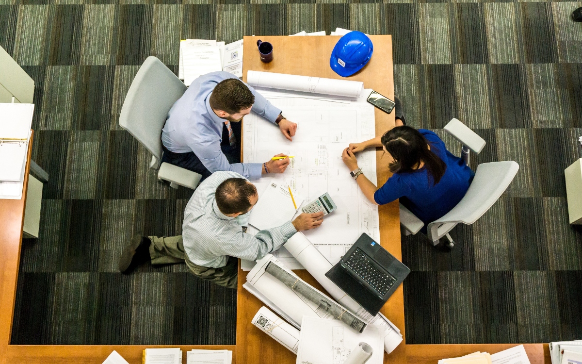 Una mesa con 3 personas trabajando juntos para un proyecto.