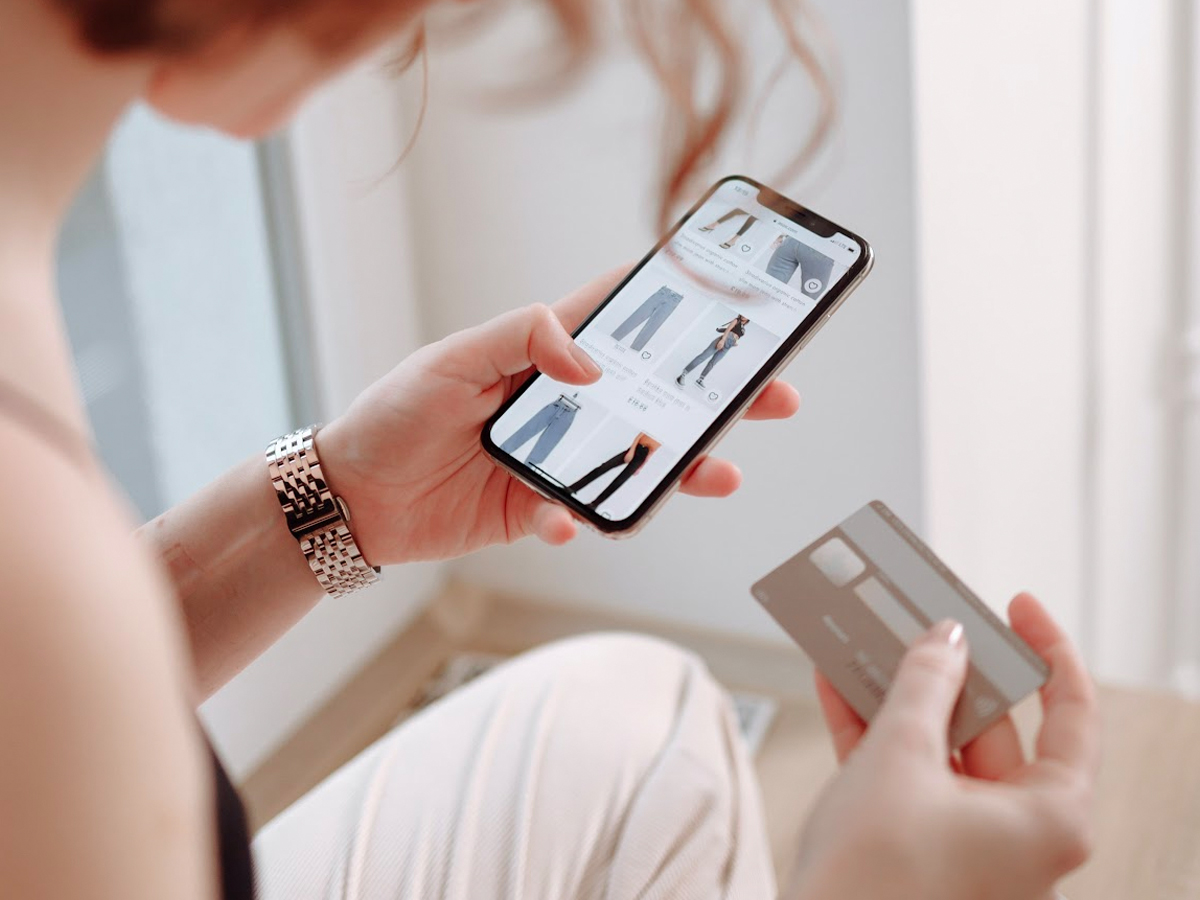 Mujer comprando ropa online en su móvil con tarjeta de credito.
