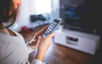 Chica mirando el teléfono en su casa controlando uno de los diferentes tipos de sistemas domóticos