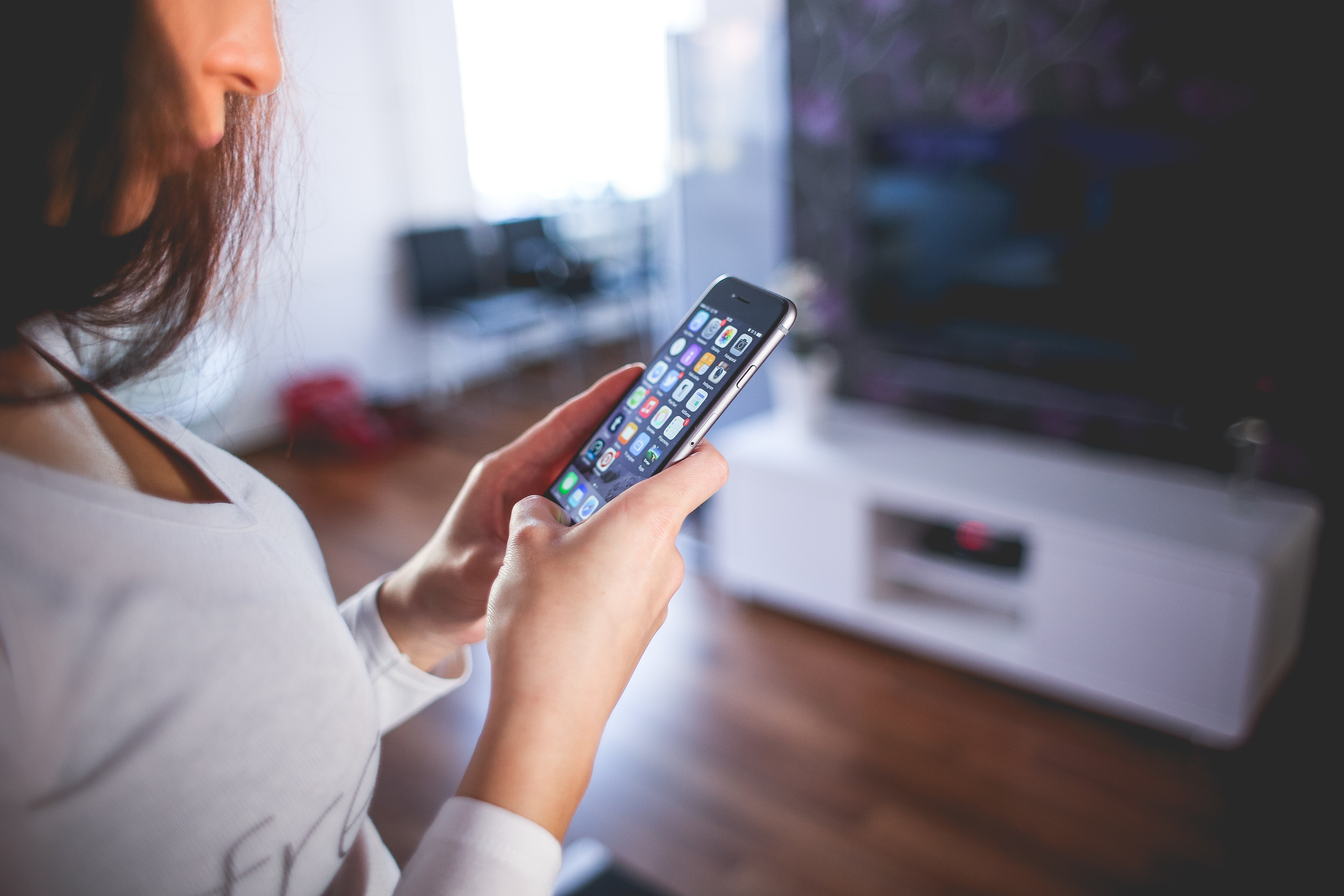 Chica mirando el teléfono en su casa controlando uno de los diferentes tipos de sistemas domóticos