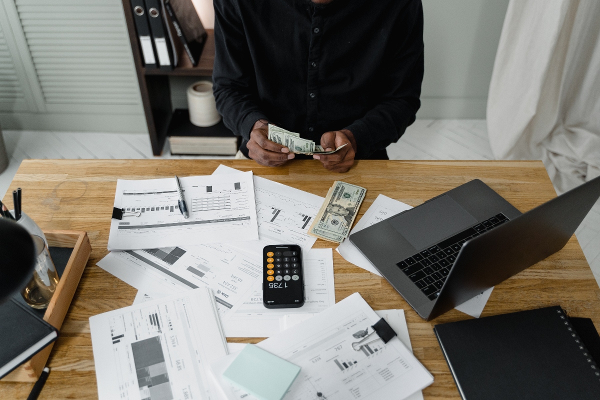 Persona contando dinero con una calculadora y papeles delante.