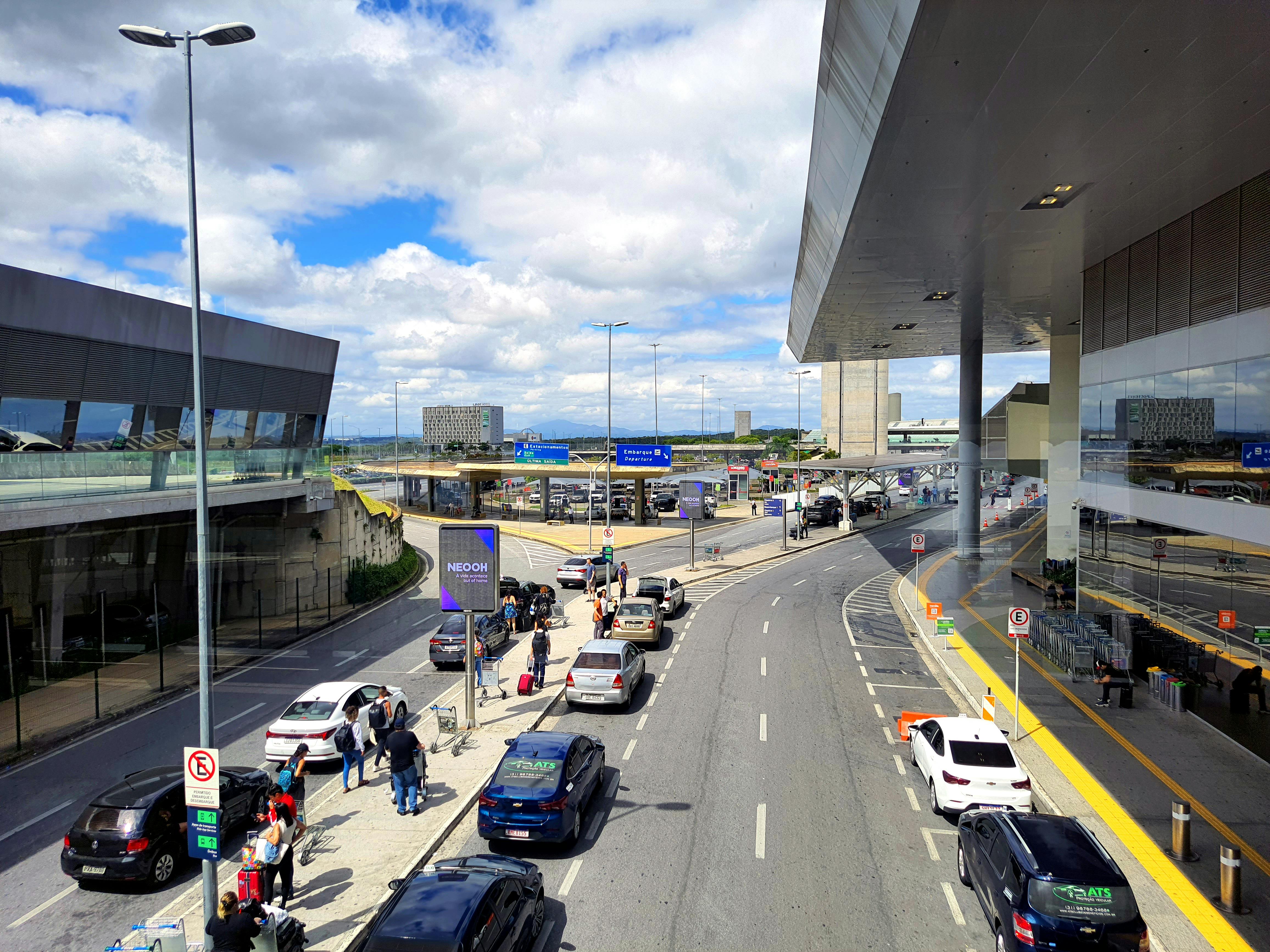 Diferencias de precio según el punto de recogida del coche de alquiler. Zona de recogida de pasajeros y vehículos en la terminal de un aeropuerto, ilustrando el ahorro al alquilar un coche en oficinas de la ciudad o las afueras en lugar del aeródromo.