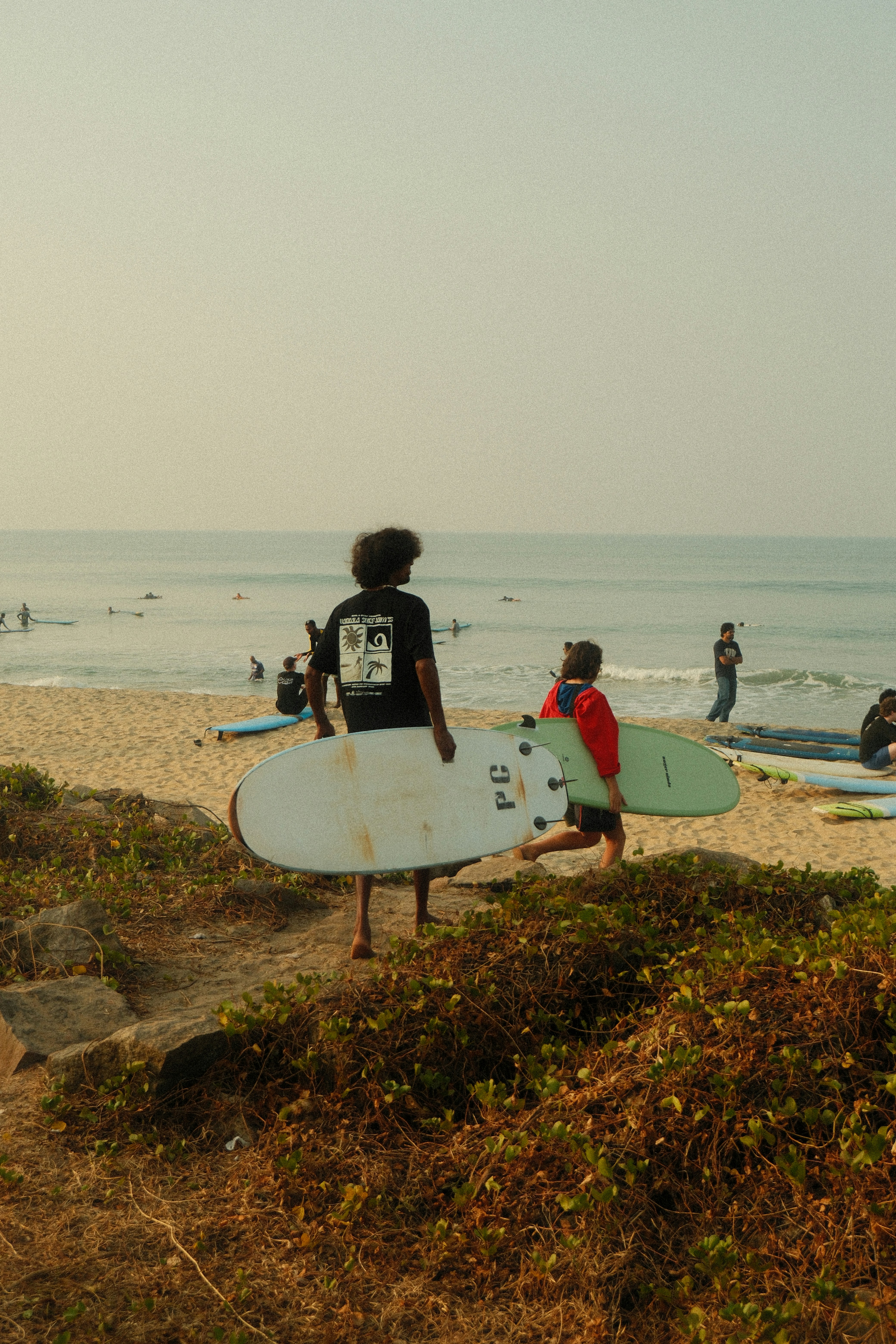 El verano es perfecto para hacer actividades como el surf Dos jóvenes llegando a la playa con tablas para tomar una clase de surf