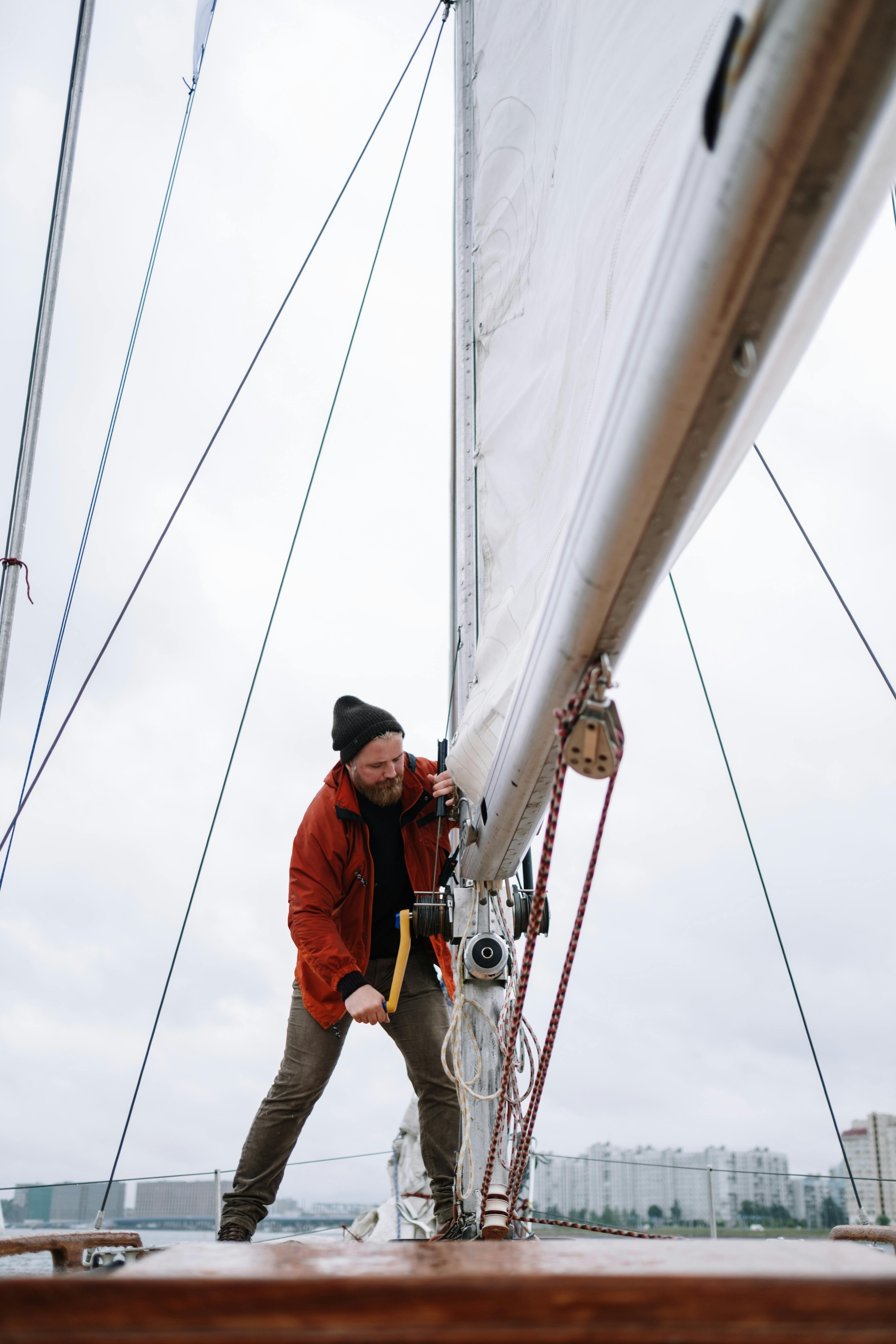 Habilitación a vela y prácticas para el título PER Un hombre ajustando el aparejo de un velero, ilustrando las prácticas requeridas para obtener el título de Patrón de Embarcaciones de Recreo (PER) y sus atribuciones.