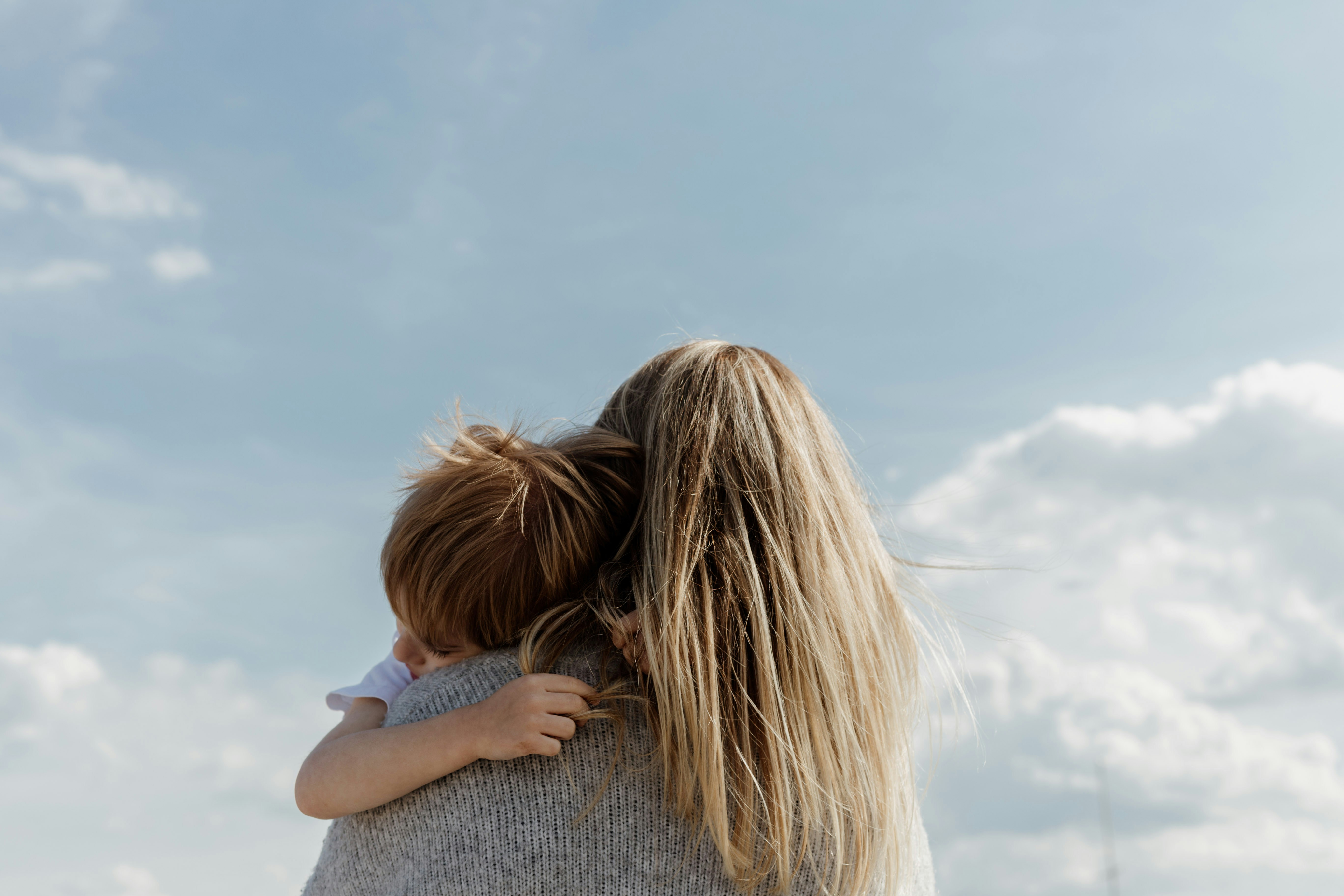 Una madre separada con su hijo en brazos Madre separada de espaldas sostiene a su hijo en brazos con el cielo de fondo