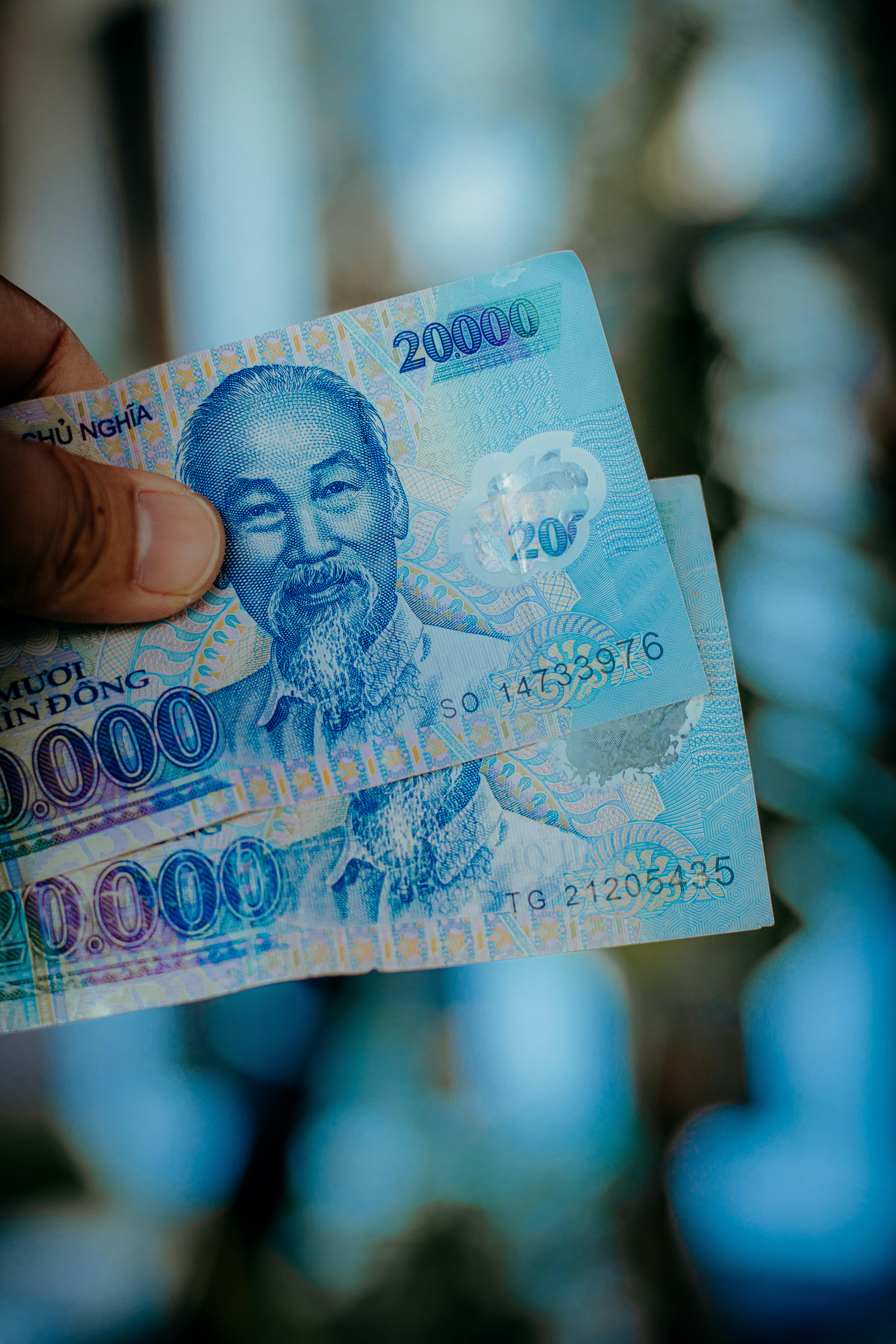 Gestión de moneda local y efectivo en Vietnam. Billetes de Dong vietnamita en mano, ilustrando el cambio de moneda y el uso de efectivo necesario para viajar a Vietnam.