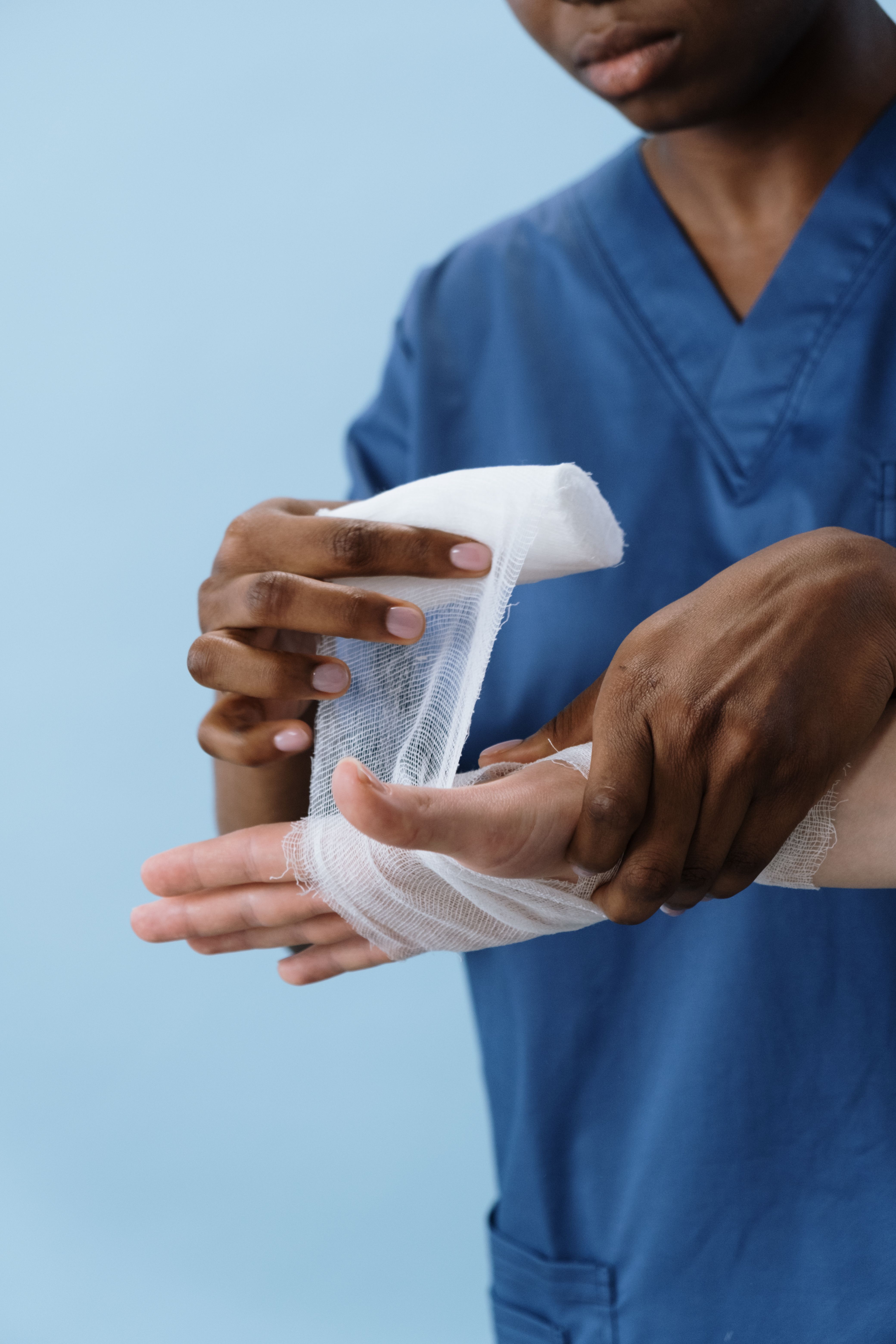 Facturas médicas y asistencia sanitaria de urgencia en el extranjero. Un profesional sanitario aplicando un vendaje de gasa en la mano de un paciente, representando la asistencia médica de urgencia que requiere una garantía de pago si se viaja sin la Tarjeta Sanitaria Europea.