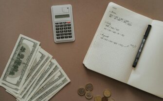 Una mesa con una libreta de gastos, unas monedas, unos billetes y una calculadora.