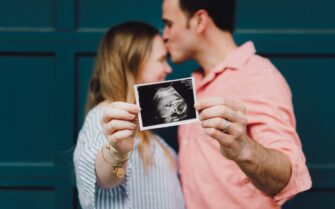 Una pareja besándose muestra la ecografía de su primer hijo