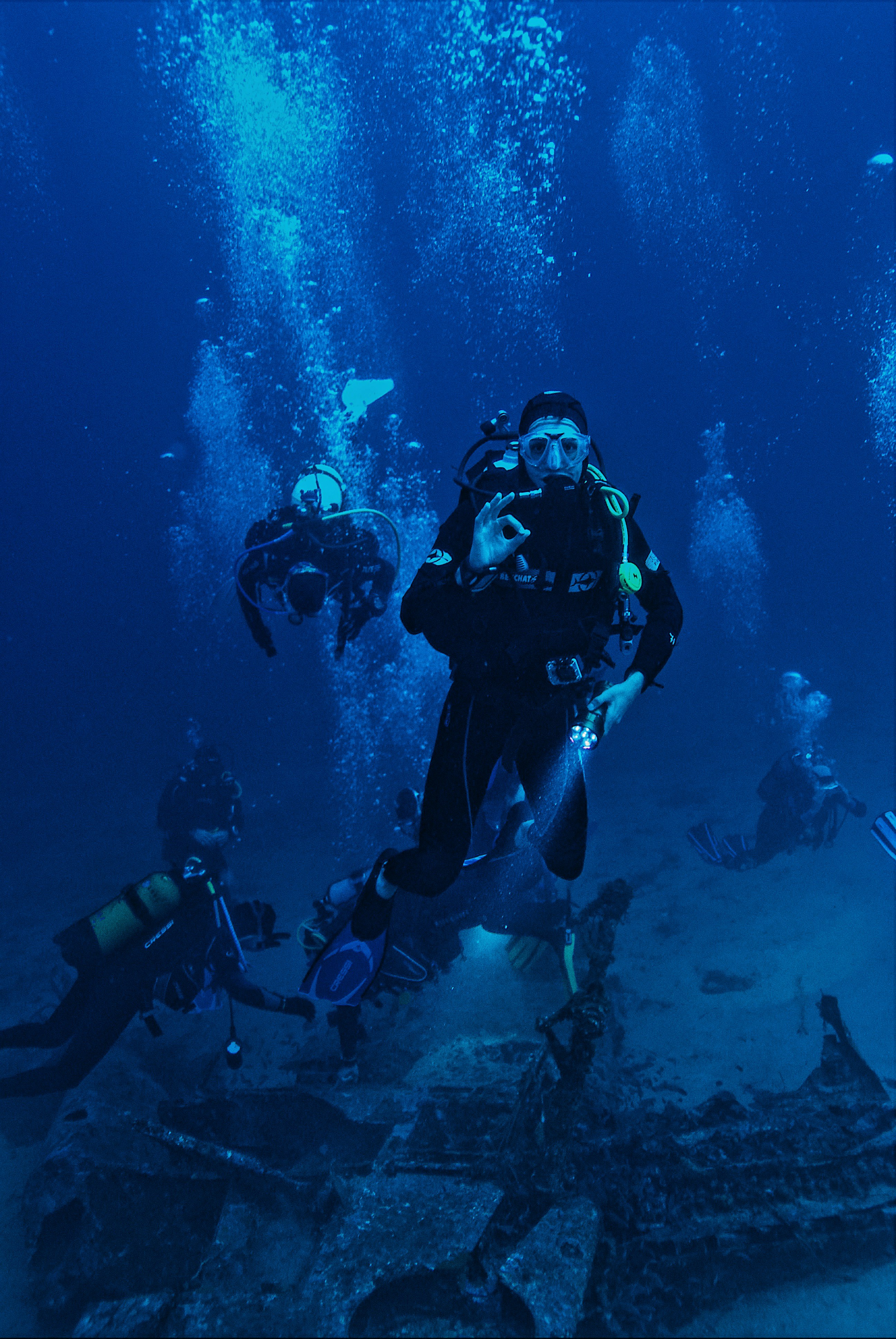 Grupo de buceadores en el fondo marino Grupo de submarinistas explora el fondo marino mientras uno señaliza que todo va bien