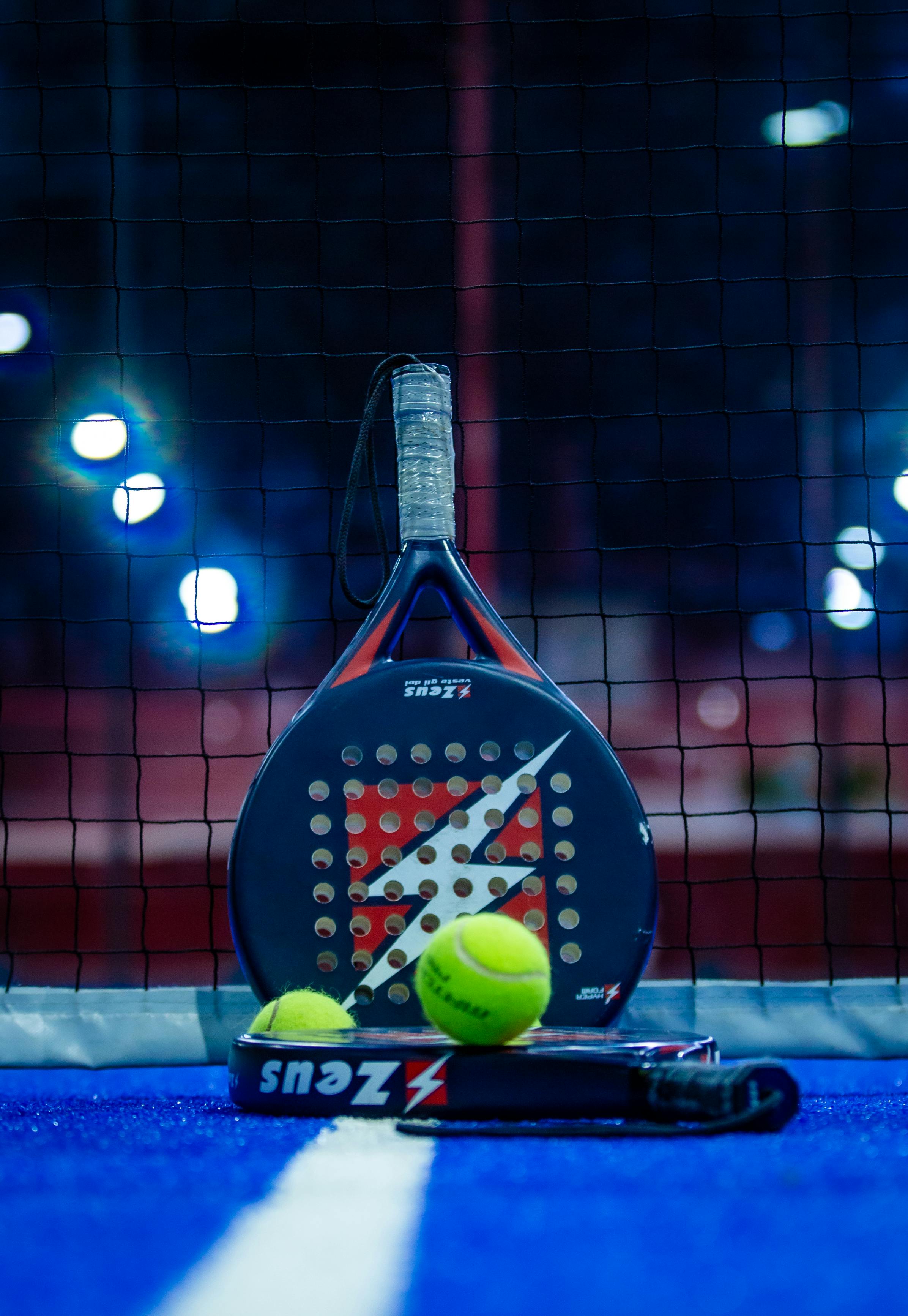 pala_para_jugar_al_padel Una pala de pádel apoyada en la red de una pista de pádel.
