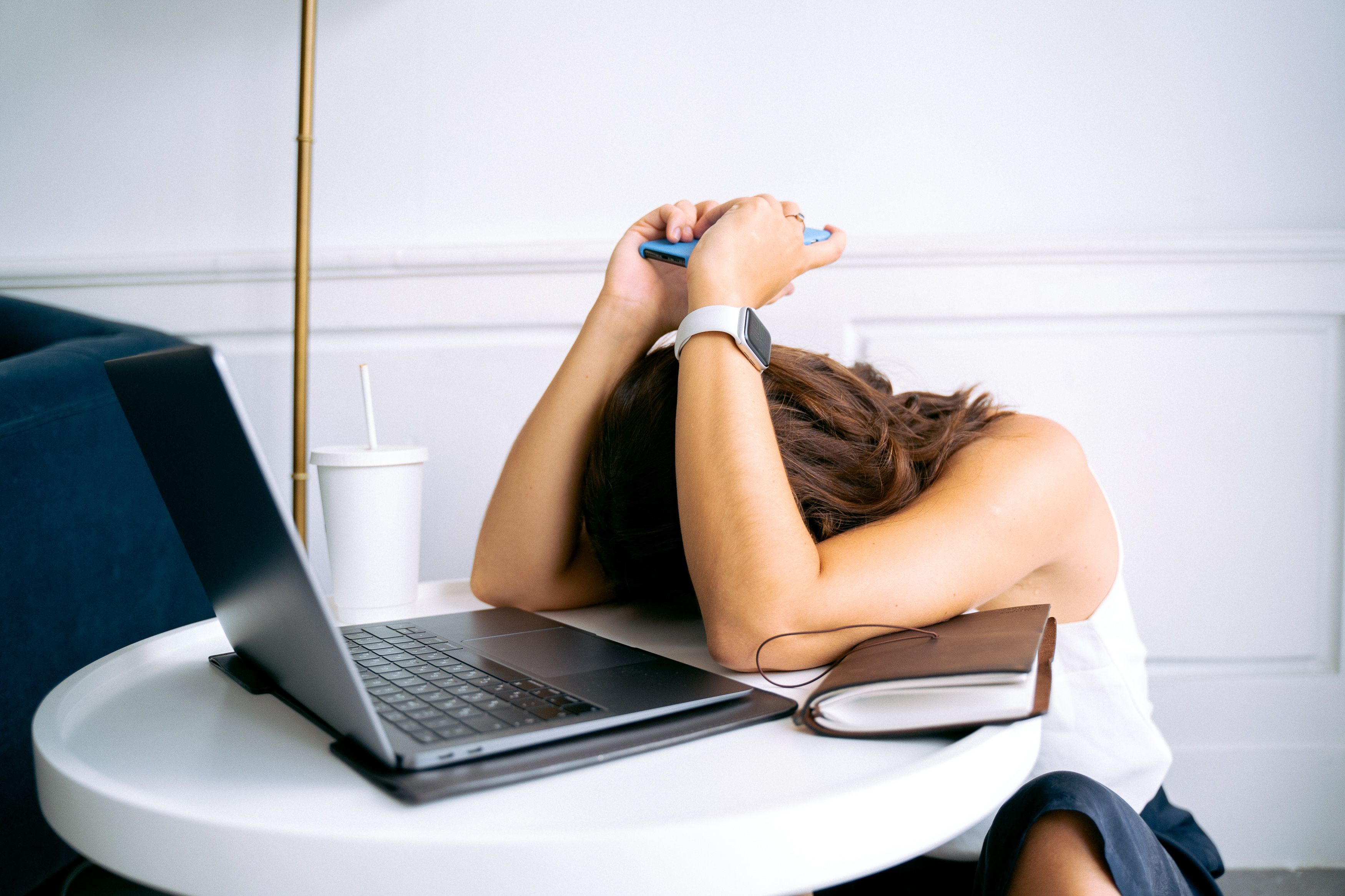 Desconexión digital y derecho al descanso laboral. Una mujer con la cabeza apoyada en la mesa sosteniendo un teléfono móvil junto a su ordenador portátil, ilustrando la necesidad de desconexión digital para evitar el agotamiento laboral.