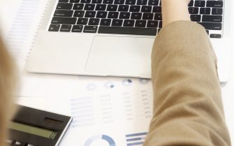 Una mano señala con un bolígrafo una tabla de gastos en la pantalla de un ordenador portátil junto a una calculadora y gráficos financieros.