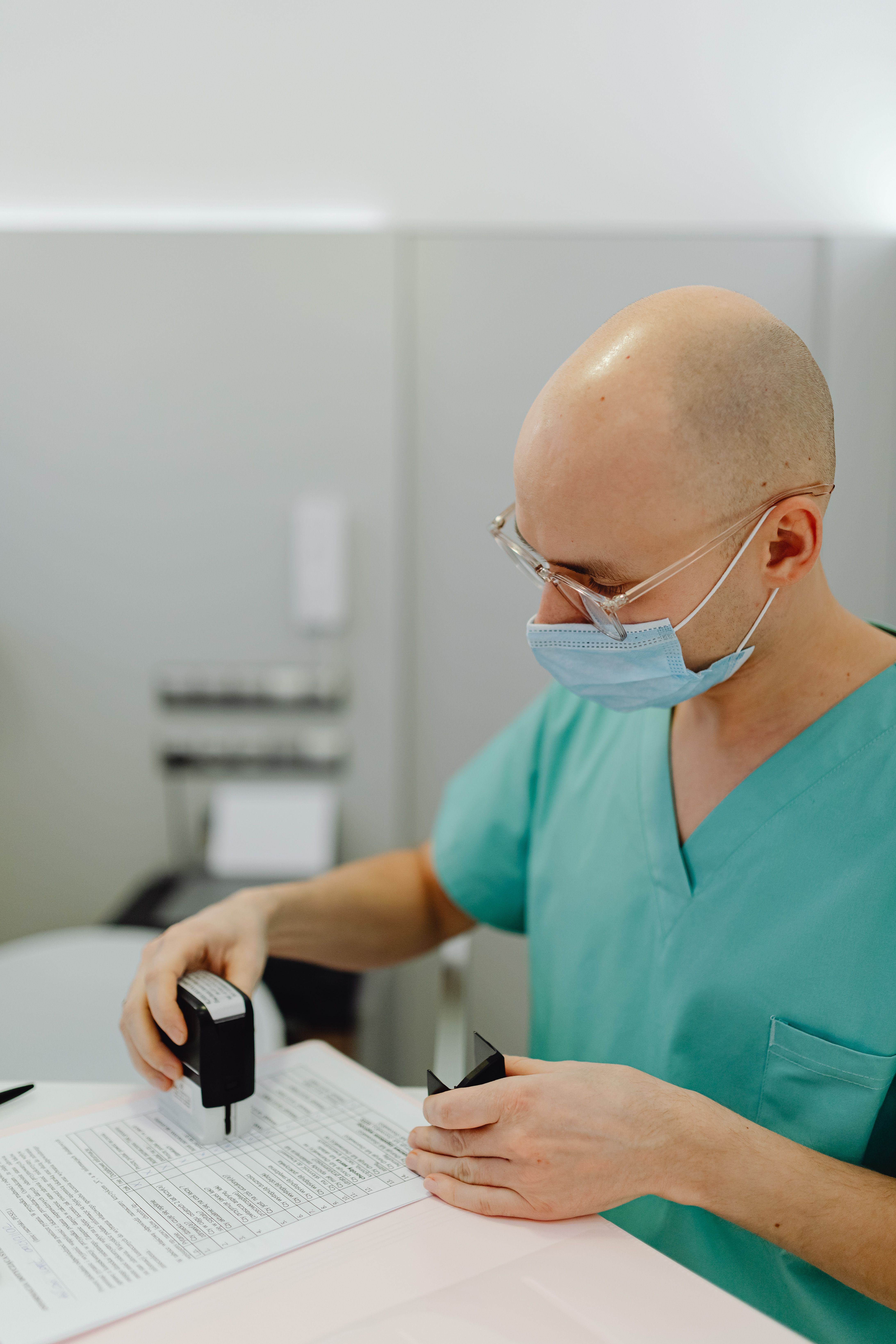 Gestión y obtención del parte de alta médica oficial. Un profesional sanitario con mascarilla y uniforme verde sellando un formulario oficial, ilustrando los pasos de cómo tramitar el alta médica tras una incapacidad temporal.