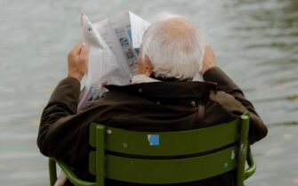 Una persona mayor sentada en una silla de jardín leyendo el periódico frente a un lago, ilustrando la tranquilidad financiera tras contratar un plan de pensiones para la jubilación.