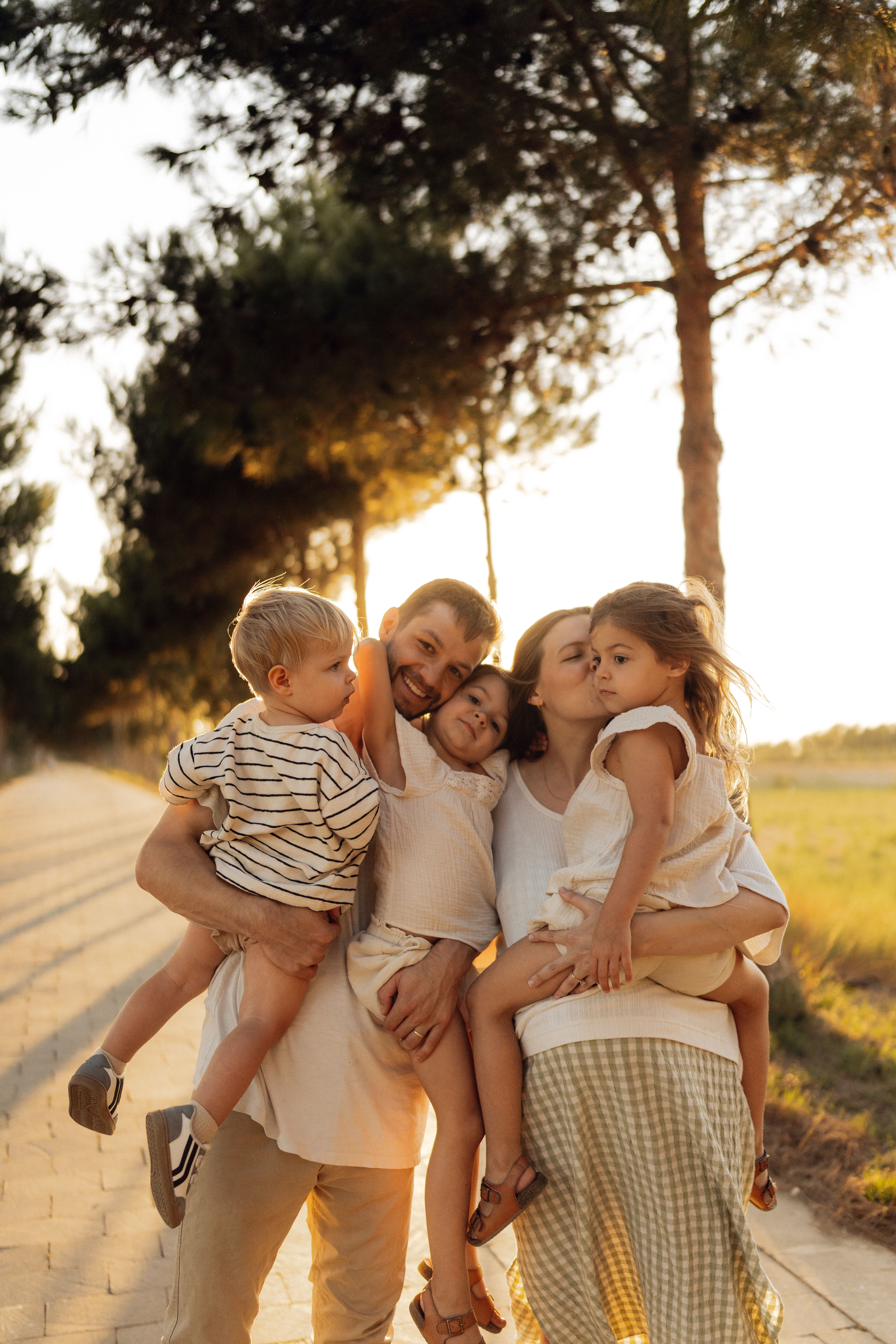 Una familia numerosa de cinco miembros en el parque Dos padres sujetan a sus tres hijos en el parque durante el atardecer