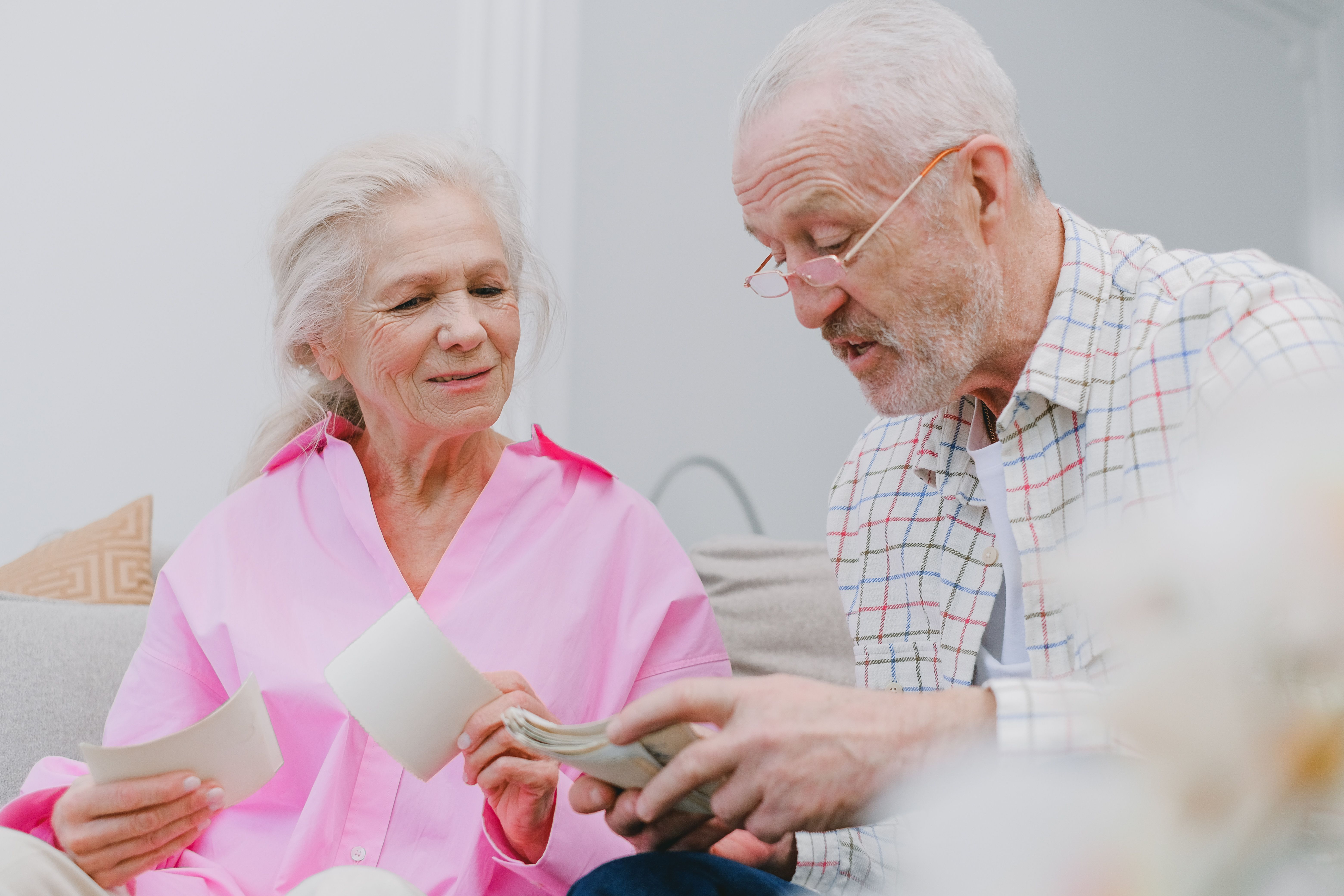 Modalidades de cobro y rescate del dinero del plan de pensiones. Una pareja de jubilados revisando billetes en el salón de su casa, representando la elección de la modalidad de rescate y cobro del capital de un plan de pensiones.
