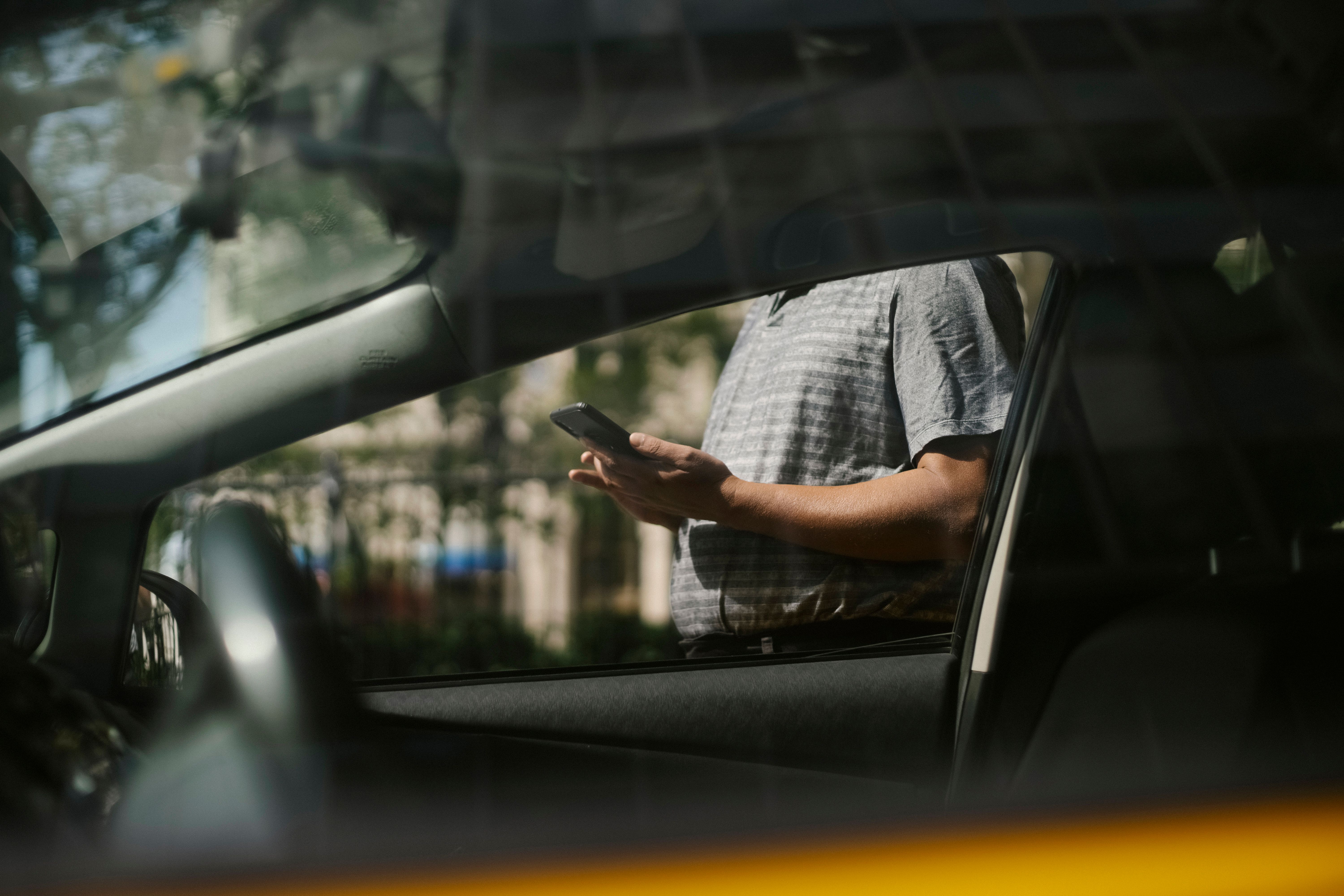 Financiación y préstamos para adquirir una licencia VTC Una persona consultando un teléfono móvil a través de la ventanilla de un vehículo.