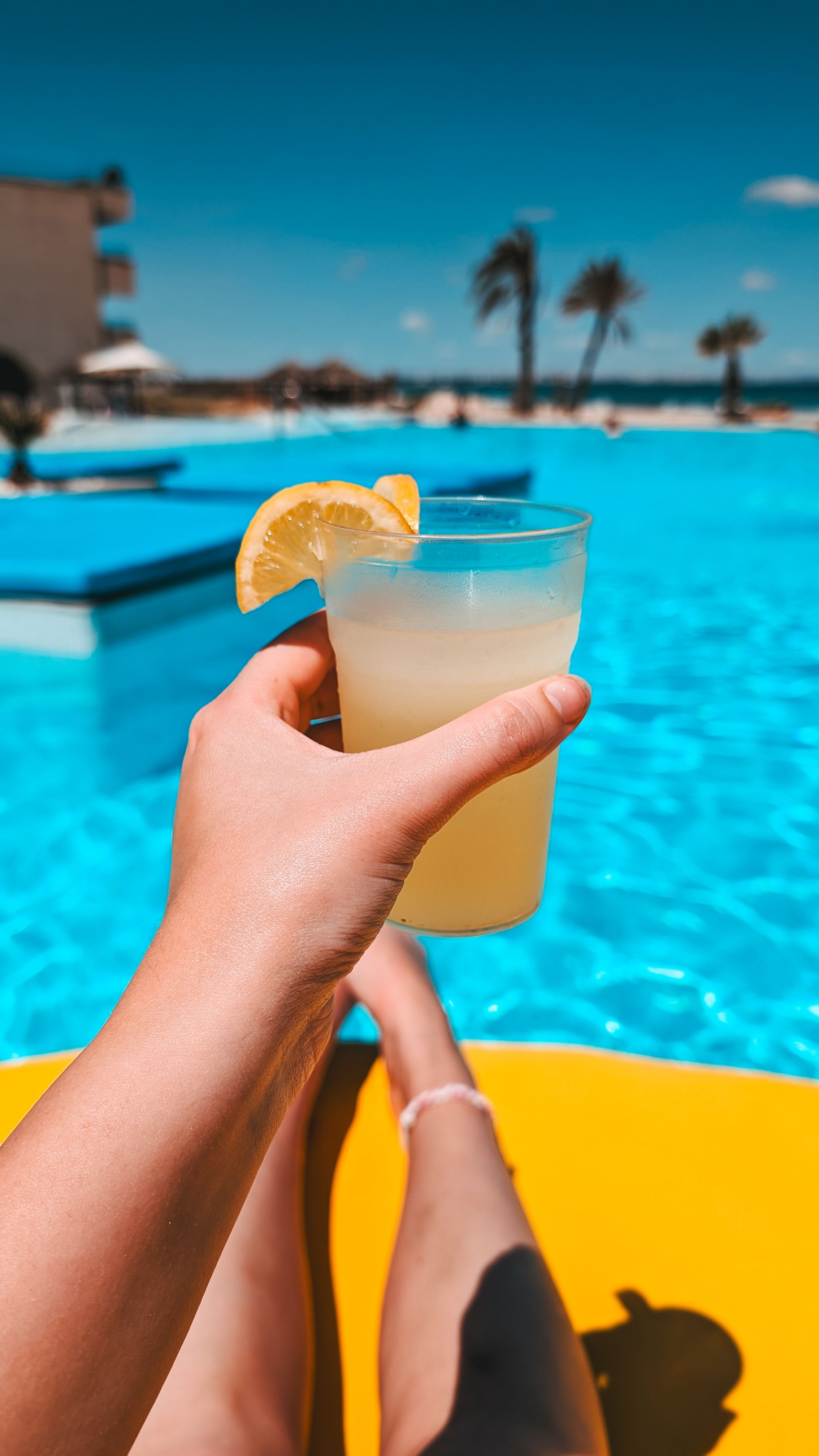 Huésped disfrutando de su hotel todo incluido Mano de una persona de vacaciones sosteniendo una limonada desde encima de un flotador en la piscina de un hotel