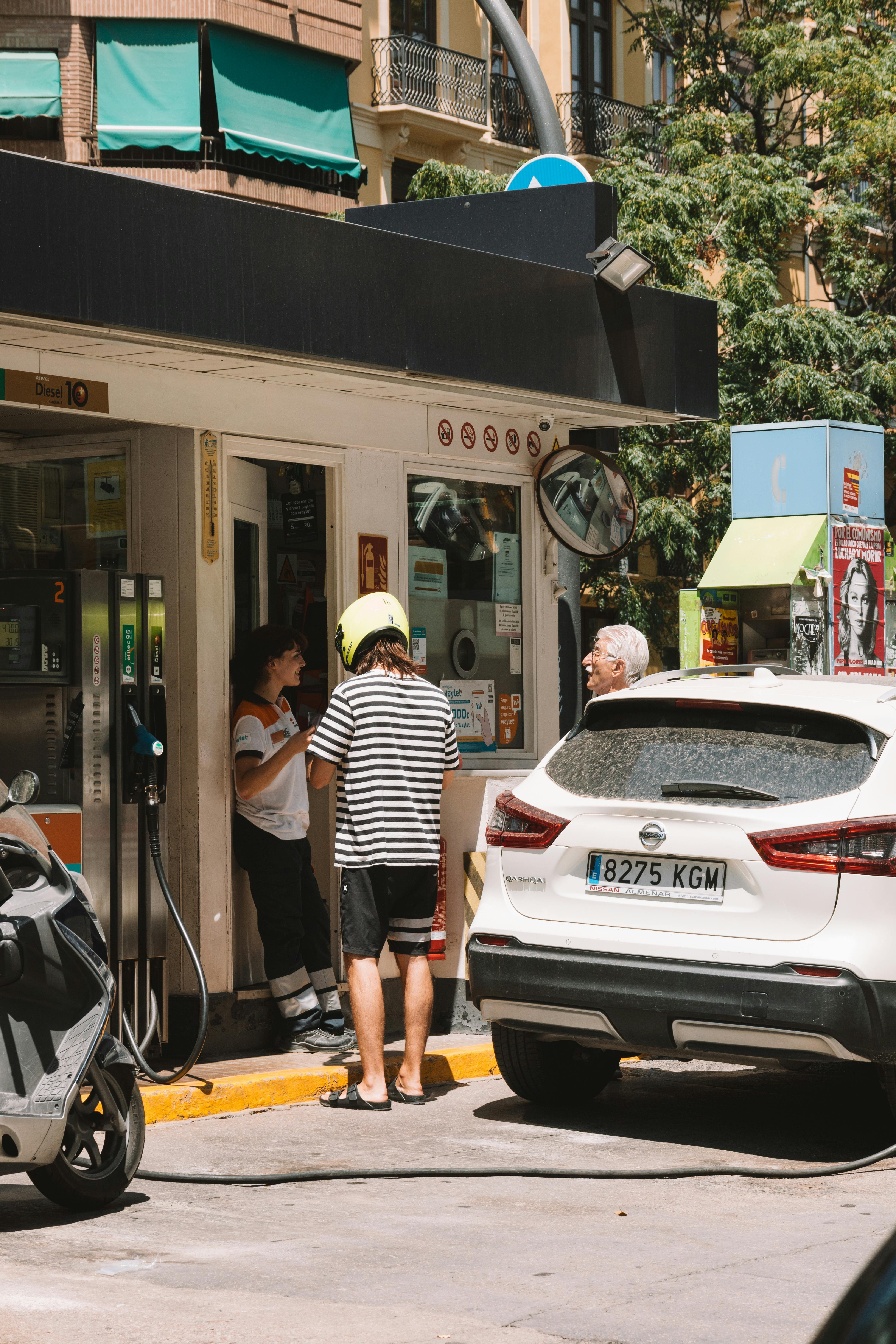Repostaje y políticas de combustible en el alquiler de vehículos. Un vehículo blanco repostando en una gasolinera, ilustrando cómo cumplir con la política de depósito lleno al devolver un coche de alquiler en vacaciones.