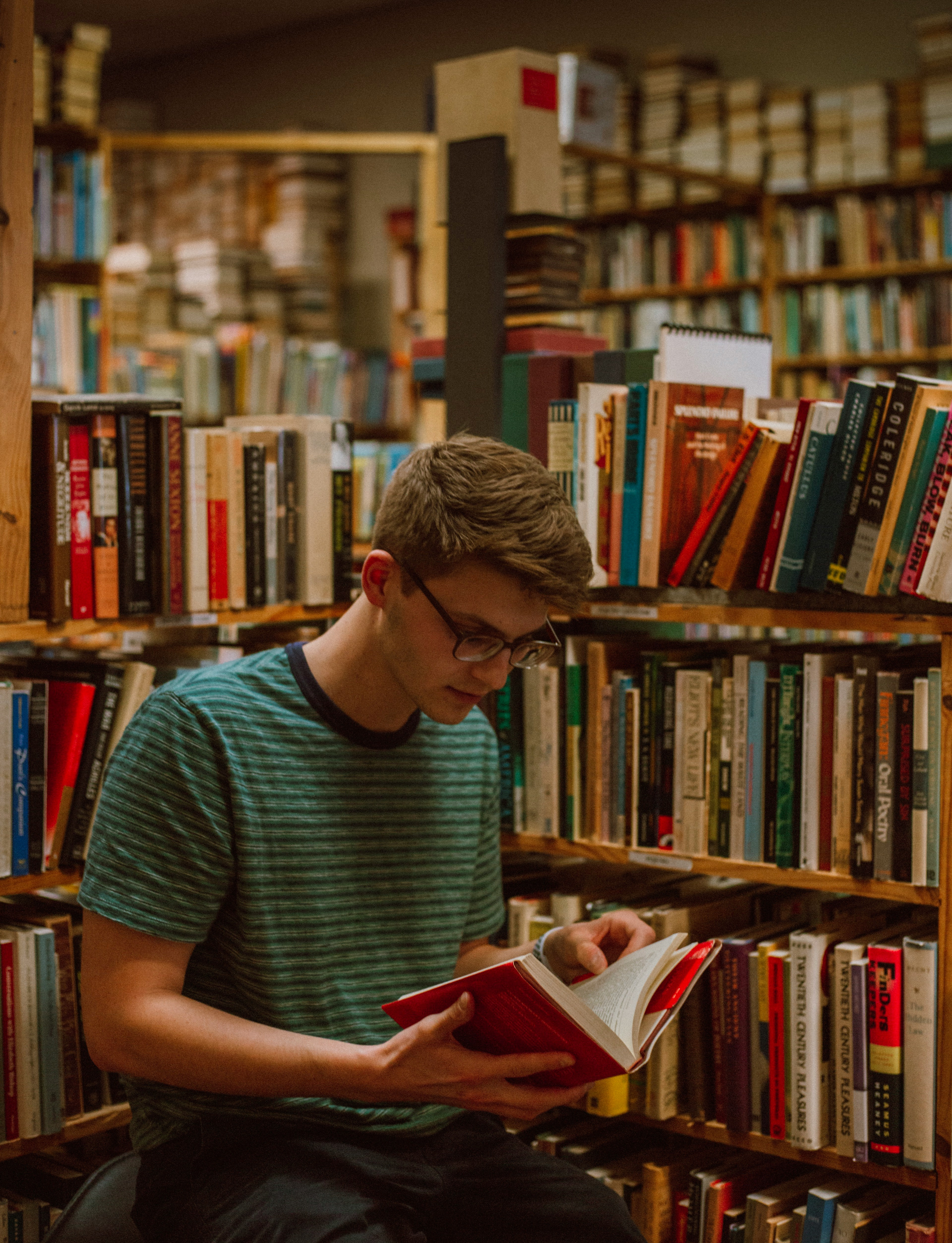 100 euros del Bono Cultural pueden dedicarse a la compra de productos culturales físicos. Un chico en una biblioteca, leyendo un libro.