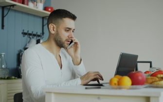 Hombre en la cocina con el ordenador y hablando por teléfono para cambiar de operador